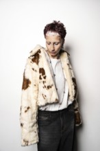 Woman in a faux fur coat poses against a white background, wearing a white shirt and dark jeans.