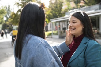 A joyful Latin lesbian couple enjoys a tender moment in a sunlit outdoor setting, expressing love