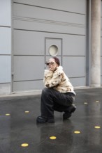 A fashionable woman wearing a fur jacket and dark jeans poses stylishly outdoors, surrounded by a