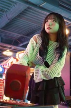 Asian Gen Z girl immersed in arcade fun, surrounded by vibrant lights and playful atmosphere Her