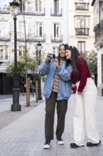 A Latin lesbian couple enjoying a day in the city, sharing a joyful moment while capturing memories