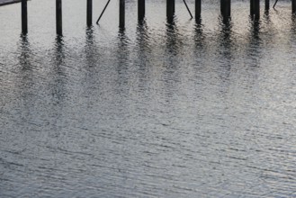 Water reflections with wooden poles standing vertically. The ripples and light reflections create a