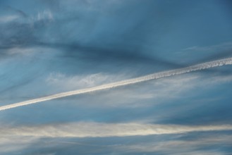 Airplane contrail across a clear blue sky. The white streak contrasts beautifully with the soft