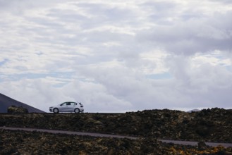 Car on a lonely road surrounded by a volcanic landscape. The rocky formations emphasize the