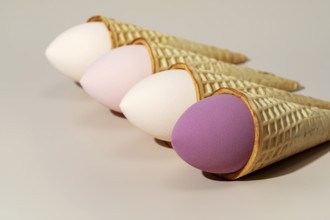 Four colorful cosmetic sponges creatively placed in ice cream cones The sponges, in pastel shades,