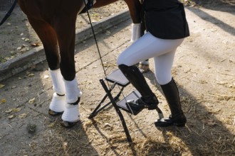 Cropped unrecognizable image of a teenager in classical dressage attire, adjusting a stirrup in