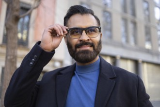 An Indian businessman in stylish winter attire, adjusting his glasses while smiling confidently