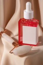 Close-up of a red serum cosmetic and a jade roller on soft beige fabric The composition highlights