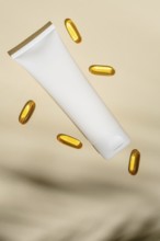 Top view of a blank white cosmetic tube floats amidst golden oil capsules, all set against a soft