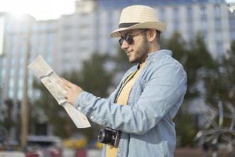 A Latino transgender man in a hat and sunglasses explores a city with a map and camera, embracing