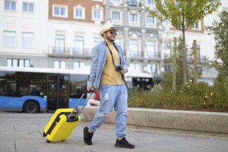 A stylish Latino transgender man strolls through the city with a camera and a vibrant yellow