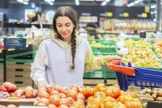 A happy young woman picking tomatoes from a stall in a supermarket, examining them carefully while