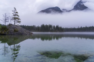 A quiet morning at Hintersee, with mist over the lake reflecting trees and mountains The