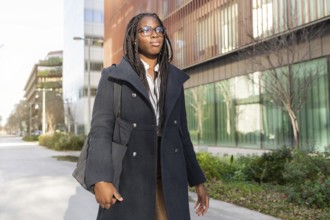 African American businesswoman with braided hair dressed in a stylish coat, takes a break outdoors
