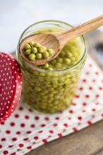 Close up of vibrant green homemade organic peas in a glass jar, with a wooden spoon resting on top.