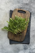 Bunch of fresh arugula placed on a rustic wooden cutting board with a dark cloth, set against a