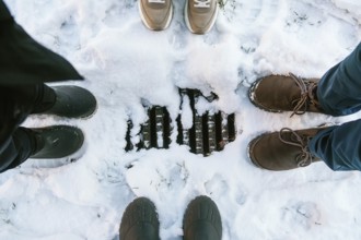 Four pairs of shoes and boots encircle a snow-covered drain in Stockholm, capturing a cozy glimpse