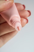 Cropped unrecognizable woman's hand applying a shiny lip balm from a pink tube, showcasing cosmetic