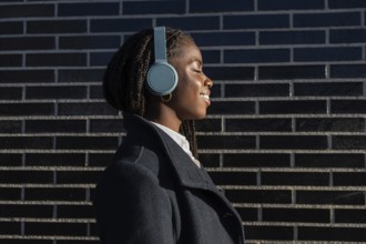 African American businesswoman with braids smiles while listening to music with headphones during a