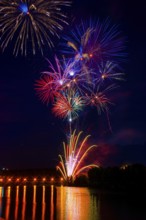 Vibrant fireworks illuminate the night sky above the Ebro River, reflecting on its calm waters. The