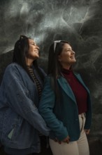 A joyful Latin lesbian couple shares a heartfelt moment, smiling warmly. They are dressed