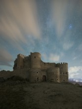 The medieval Manqueospese Castle in Avila, Spain, stands under a starry sky, with ethereal clouds
