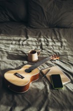 A cozy and creative setting featuring a ukulele, a ceramic mug, an open notebook with a pen, and a