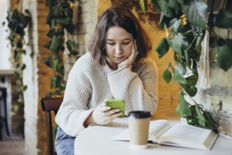 A young woman in a relaxed sweater sits at a table in a bookstore cafe, resting her head on her