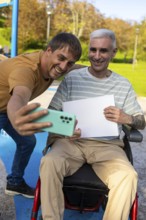 Two friends in a park enjoy taking a selfie together One person is sitting in a wheelchair by