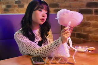 Young Asian Gen Z girl enjoys a vibrant arcade environment, sitting at a colorful booth with cotton