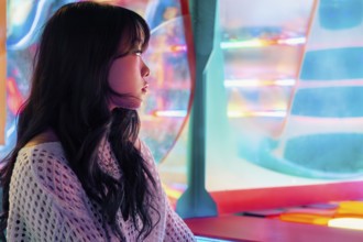 A young Asian Gen Z girl enjoys vivid lights and colors in an arcade, capturing the essence of