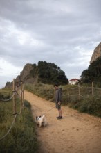 A serene scene of a man walking his dog along a sandy path in Ea, Basque Country, Spain The pathway