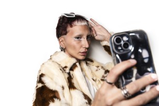 Stylish woman with bold eye makeup and piercings takes a selfie wearing a fur coat and sunglasses.