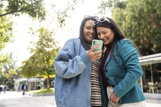 A joyous latin lesbian couple is seen sharing a heartwarming moment outdoors, smiling at a phone