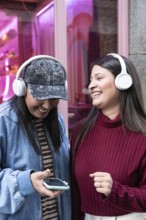 A latin lesbian couple enjoys music together with headphones. Smiling and relaxed, they share a