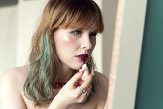 A woman carefully applies bright pink lipstick in a well-lit room Her wavy hair is styled casually,
