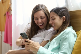 A joyful lesbian couple relaxes together while looking at a smartphone, sharing laughter and