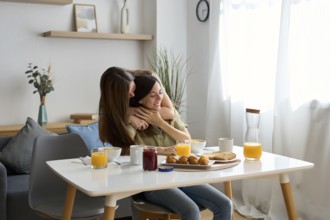 A loving lesbian couple shares a tender embrace while enjoying breakfast at a sunlit dining table