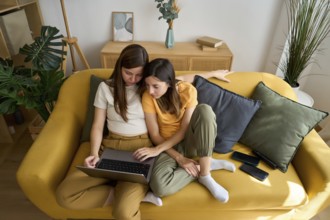 A warm scene captures a lesbian couple sharing a laptop on a cozy couch They seem comfortable and