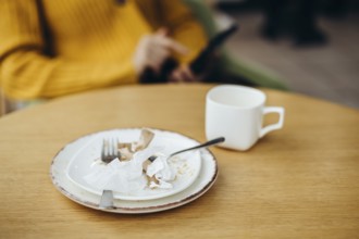 A cozy coffee shop setting featuring a wooden table with a used cup and plate Crumpled paper