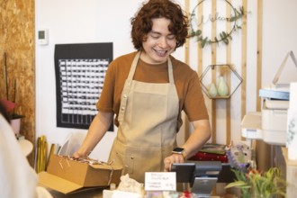 A friendly shop employee in an apron packages an order at the counter, surrounded by warm decor The