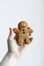 A hand holding a cheerful gingerbread man cookie, decorated with white and red icing, isolated