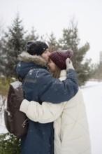 A man lovingly kisses a woman on the forehead as they embrace in a snowy park Dressed in winter