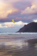 A kite surfer glides across the waves at Famara Beach, Lanzarote, under a sky painted with stunning