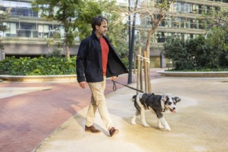 A mature man strolls with a dog through an urban park, both enjoying a sunny day. They are