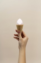 A hand holding a waffle cone with a cosmetic sponge inside, set against a soft, neutral background