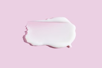 A dollop of white cream or gel cosmetic product smeared on a pastel pink background, depicting a