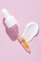 A dropper dispenses golden serum beside a white cream smear on a vibrant pink surface, representing