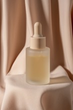 A minimalist frosted glass bottle with a dropper, containing skincare serum, is placed against