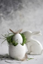 A meticulously crafted Easter setting featuring a white speckled egg cradling a nest of fresh green